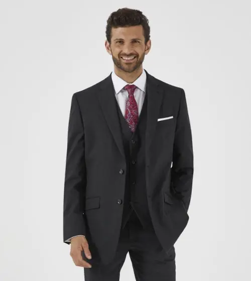 Man in a black suit with a white shirt, red tie, and white pocket square, posing for a formal wear photo.